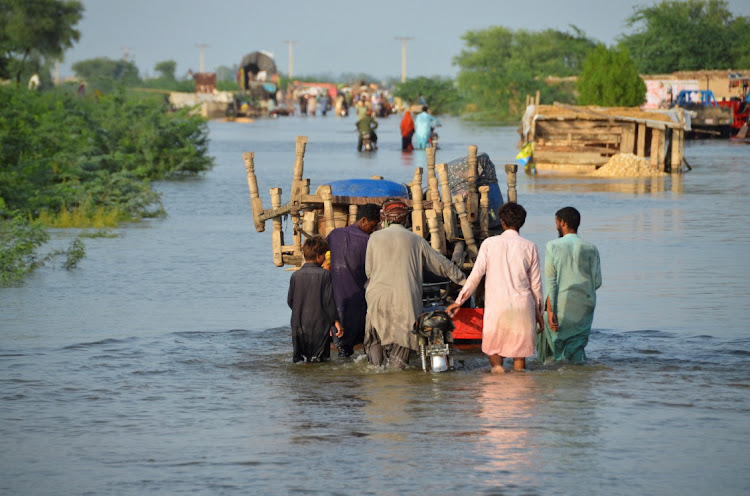 Men walk along a flooded road with their belongings, following rains and floods during the monsoon season in Suhbatpur, Pakistan, August 28 2022. Picture: REUTERS/AMER HUSSAIN