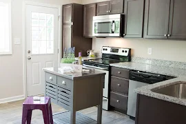 Up close view of kitchen with granite countertops, stainless steel appliances, dark brown cabinets, island, and exterior door