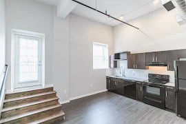 Kitchen view with high ceilings, kitchen window, steps with railing leading to an outdoor balcony, grey walls, and white trim