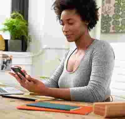 A woman seated at a desk, using an Android phone.