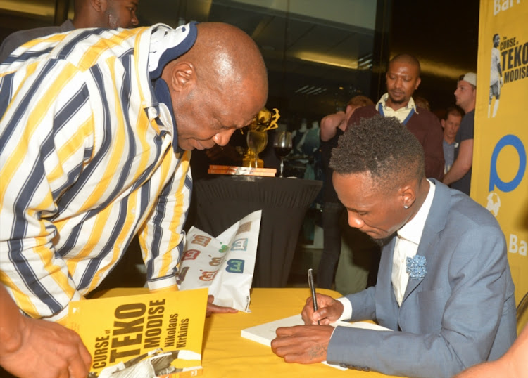 Teko Modise seen here signing his book,The Curse of Teko Modise to former Bafana Bafana coach Shakes Mashaba at the launch of it.