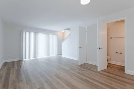 Living room with a large sliding glass door with vertical blinds next to a staircase, and a door leading to a bathroom