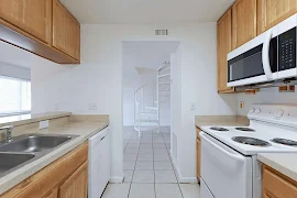 Kitchen with wood cabinets, white appliances, and staircase in the background.