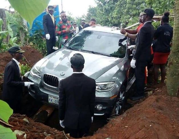 The pallbearers lower the brand new BMW into the grave as the family says their final goodbye to the patriarch.