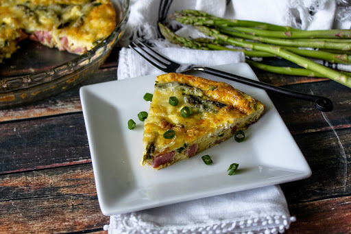 A slice of baked egg frittata on a plate with scallions sprinkled around.