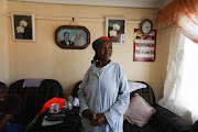 Johanna Marokane poses for a portrait in her home in Mzimhlope, Orlando West in front of a photo on the wall of father Samson and mother Magdalene. Son Matome Marokane (partly obscured) is on the left.