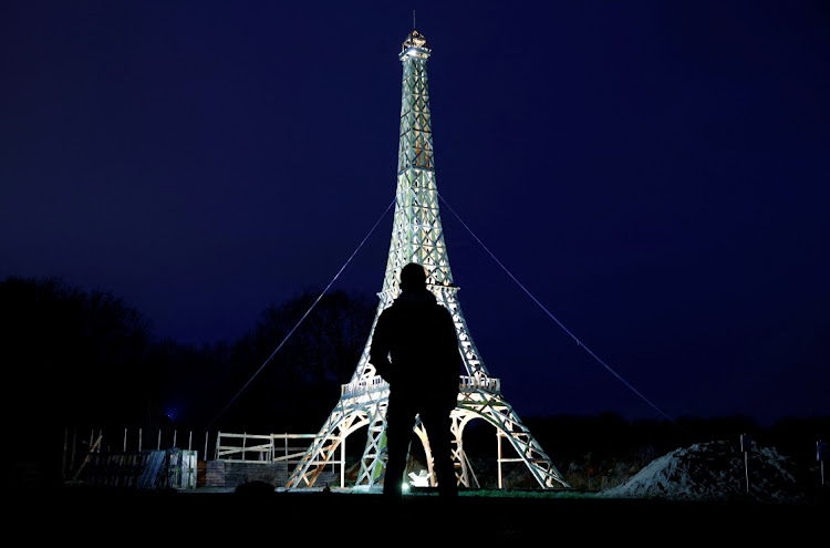 A man stands in front of a 16-meter replica of the Eiffel Tower from recycled wood built by French carpenter Frederic Malmezac and Sylvain Bouchard, a sports enthusiast with disability, which they hope to display along the path of the Olympic torch relay and in Olympic sites for the Paris 2024 Olympic and Paralympic Games, in La Chevroliere, near Nantes, France, February 19, 2024.