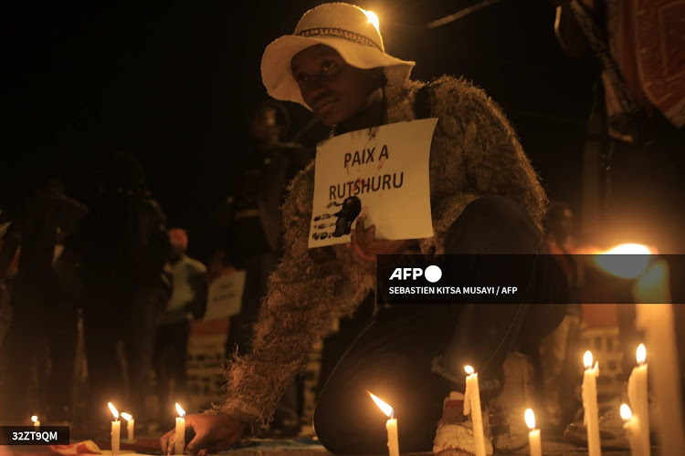 TOPSHOT - A woman places a candle in Beni on December 7, 2022 during a prayer vigil in remembrance of the victims of the ungoing unrest in the East of the country. At least 131 civilians were killed by M23 rebels on 29 and 30 November in eastern Democratic Republic of Congo, according to a preliminary UN investigation released overnight Wednesday to Thursday by the United Nations mission united in the DRC (Monusco). (Photo by Sébastien KITSA MUSAYI / AFP)