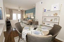 Furnished dining area facing living room with neutral and blue colored walls and wood inspired floors