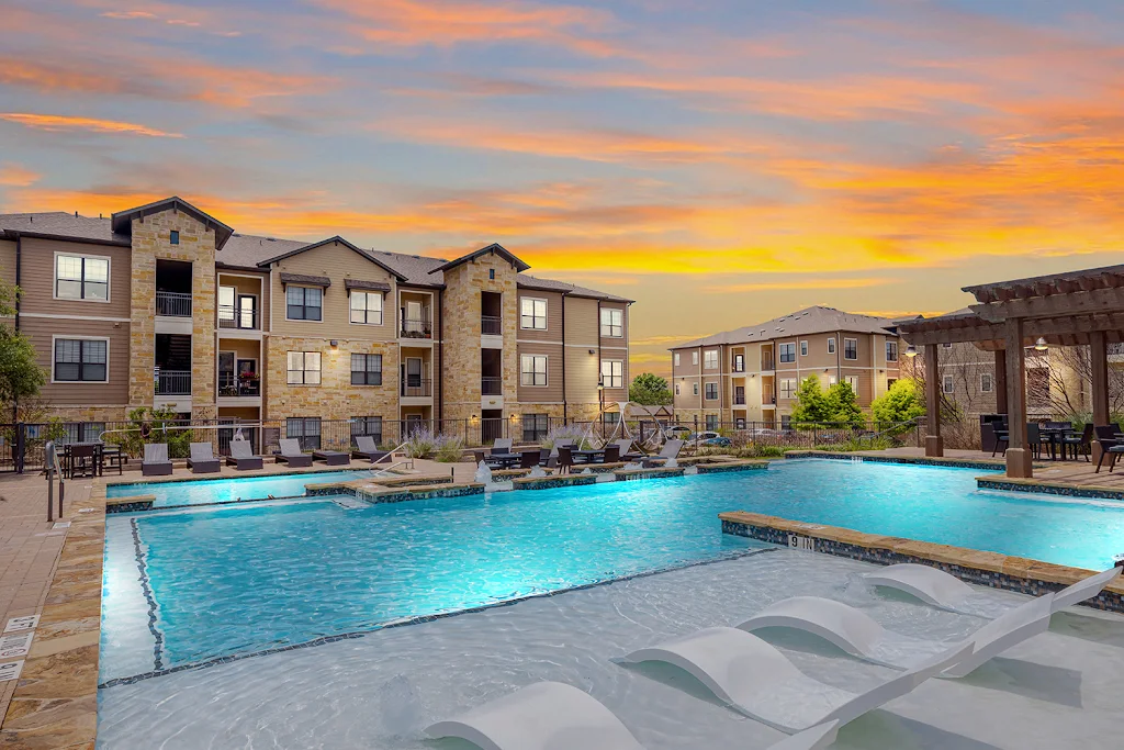 The Royce at 8100's pool at dusk with lounge chairs beside apartment buildings