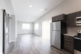 View of living room from kitchen with tall ceilings, wood plank floors, windows, gray walls, and white trim