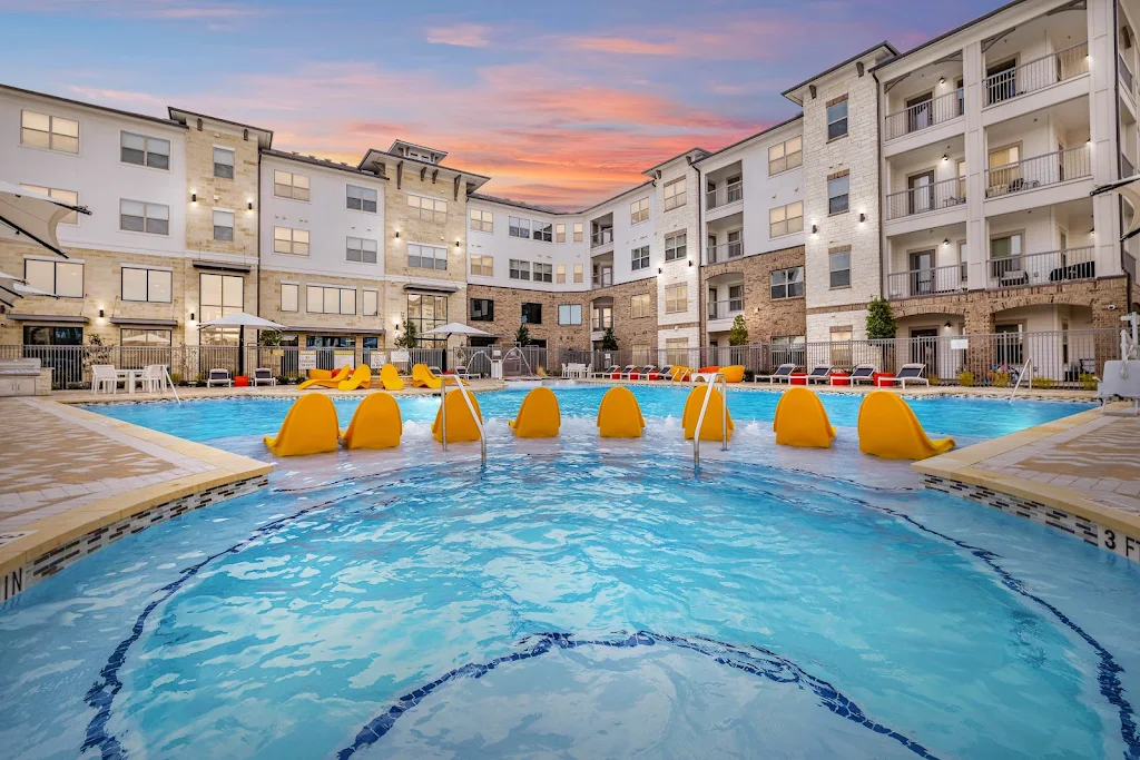 Resort-style swimming pool at dusk with orange lounge chairs and sundeck featuring a grilling station