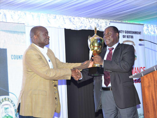 -The Kitui County Executive for Finance Simon Mundu(left) receives a trophy from Governor Julius Malombe after his department was declared tops in the 2014/15 performance. It was during the Kitui County Performance Contracts awards at the Kitui’s Ithookwe showground on Saturday night.Photo by Musembi Nzengu