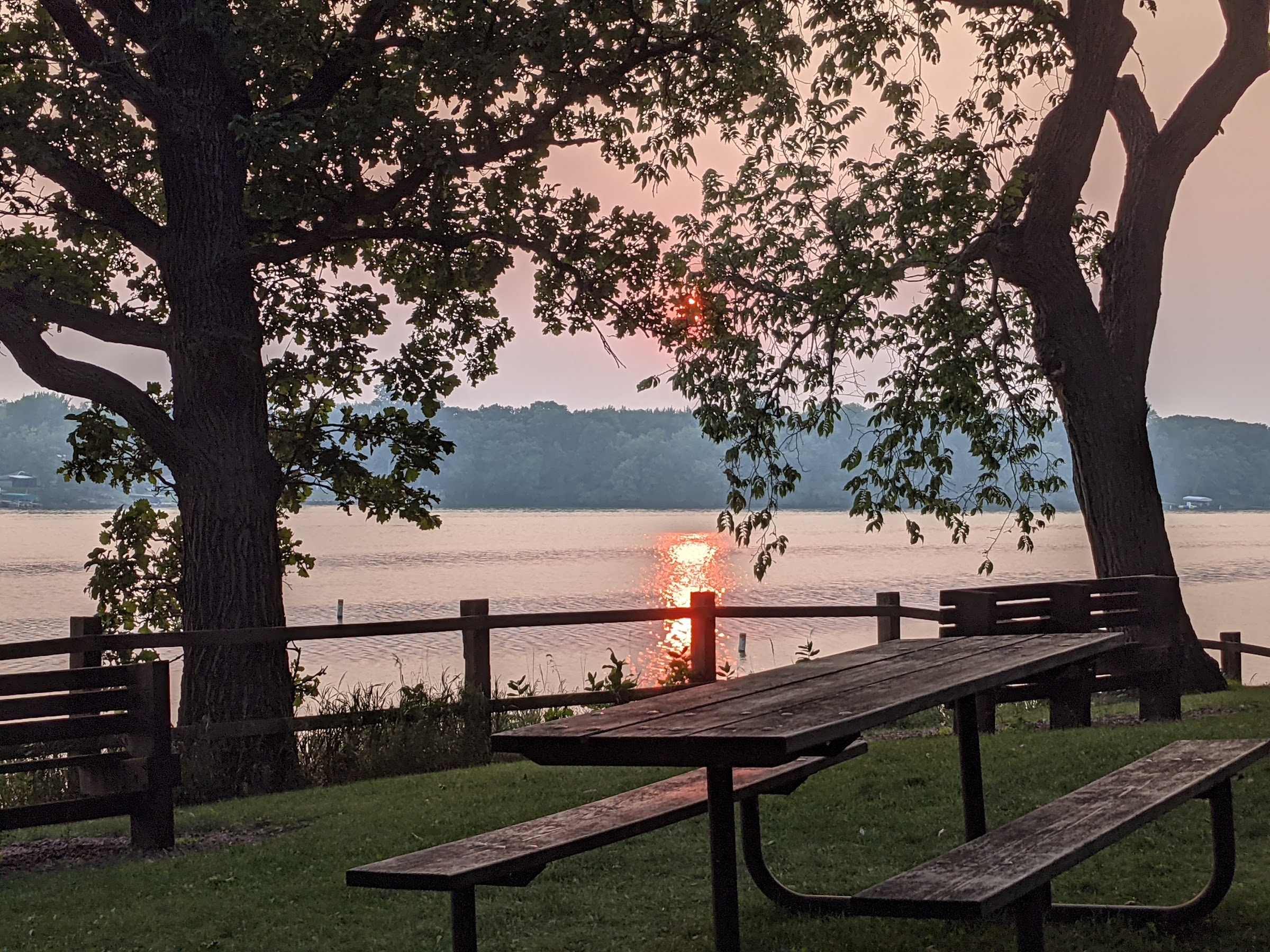 sunset in over a lake with picnic table and trees in foreground