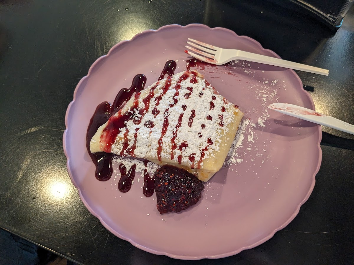 A crepe covered in powdered sugar and raspberry sauce on a pink plastic plate