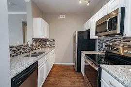 Galley-style kitchen with wood-inspired flooring, stainless steel appliances, tile backsplash, and white cabinets