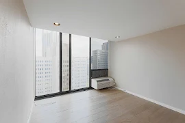 Bedroom with wood-inspired flooring, light walls, large windows with a view of the city and wall unit for temperature control