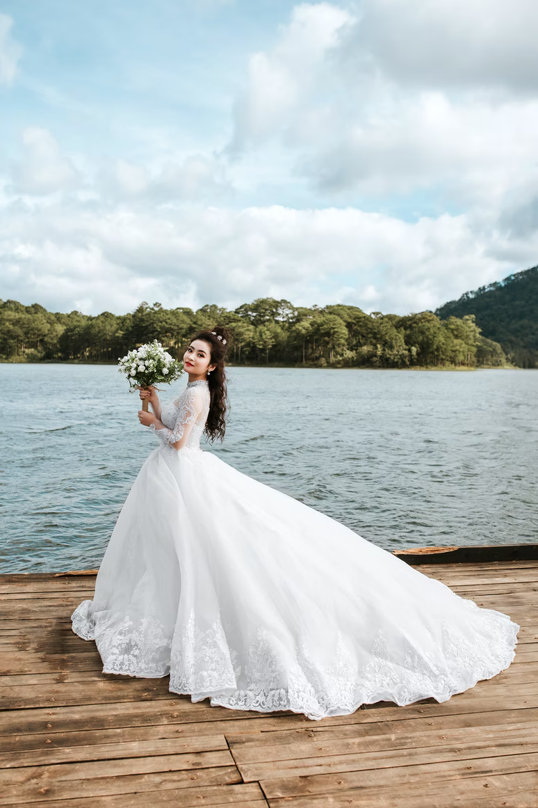 bride in white dress with white bouquet on dock in front of lake