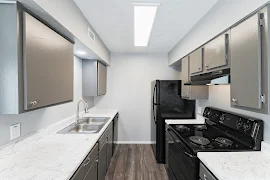 Galley kitchen with black appliances, grey cabinets, stone-inspired counters, wood plank floor