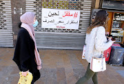 Women walk past a closed shopping centre in Sidon, Lebanon, on March 16 2021. The Arabic reads: 