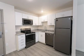 Kitchen with stone countertops, stainless steel appliances, white cabinets, and wood-inspired flooring