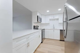 Modern apartment kitchen with white cabinetry, stainless steel appliances, and light wood flooring.