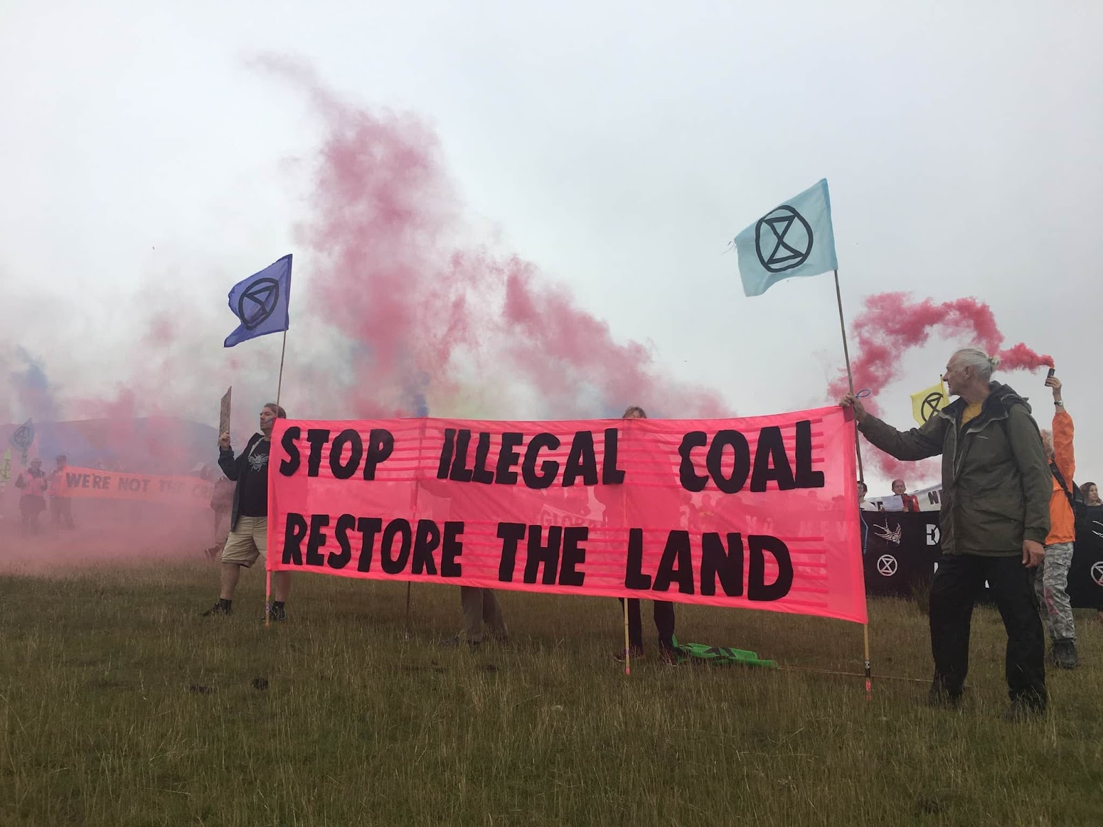 Marches hold a XR flags and a giant banner that reads 'Stop illegal coal, restore the land'.