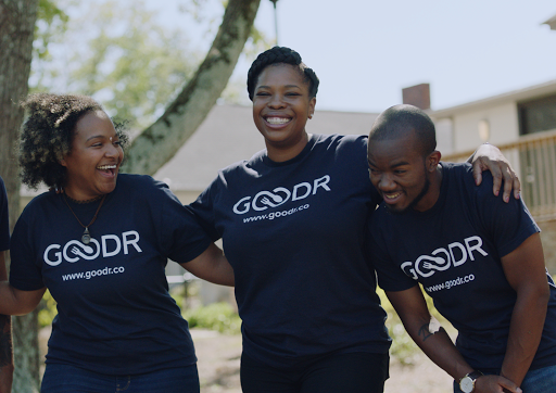 Group of coworkers wearing matching shirts smiling and holding shoulders