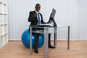 Businessman working and sitting on a pilates ball.