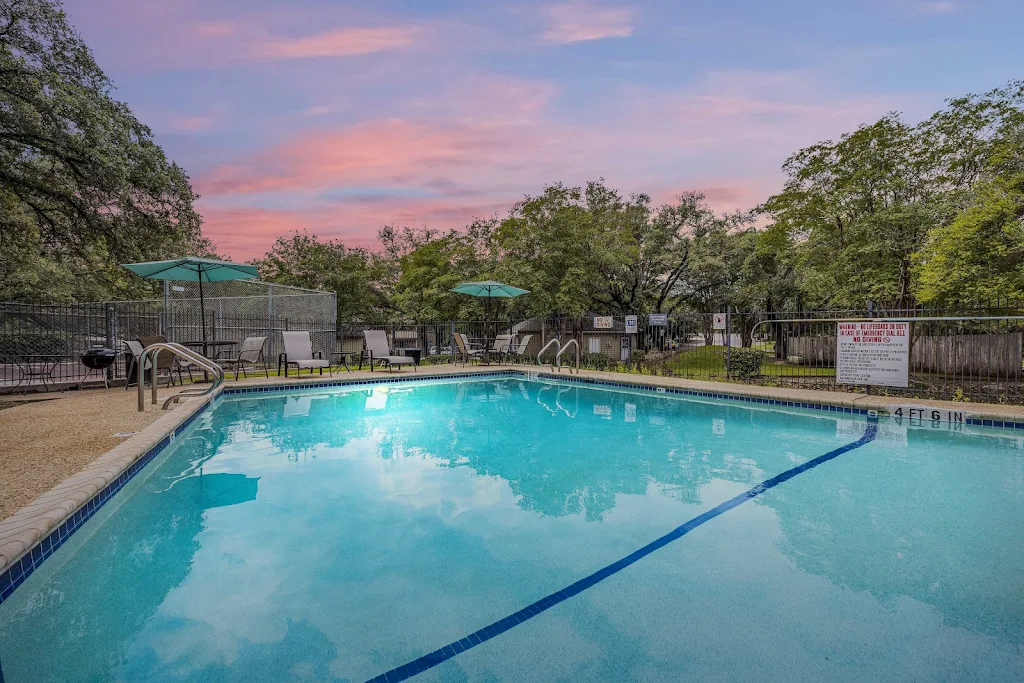 Low view of pool at dusk surrounded by patio area with chairs and umbrellas.