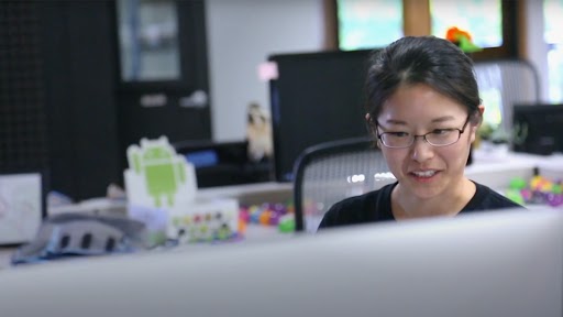 Asian woman wearing glasses sitting in front of a computer in an office.