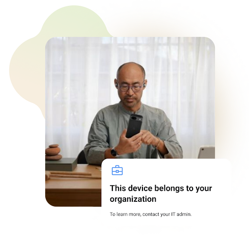 En man använder en smartphone medan han sitter vid ett skrivbord. De verkar vara på ett hemmakontor eller en arbetsplats. På skärmen står det: ”Den här enheten tillhör organisationen. Kontakta IT-administratören om du vill veta mer.”