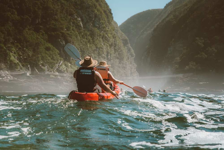 Untouched Adventures visitors paddling in over the sunlit swell before you enter the mouth of the Storms River under the suspension bridge