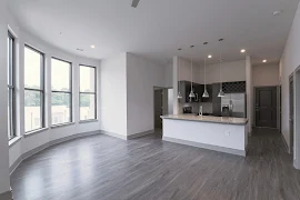 Living room with high ceilings, large windows, wood-inspired flooring, and access to the kitchen area