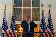 U.S. President Donald Trump removes his protective mask on the Truman Balcony of the White House in Washington, D.C., U.S., on Monday, Oct. 5, 2020. 