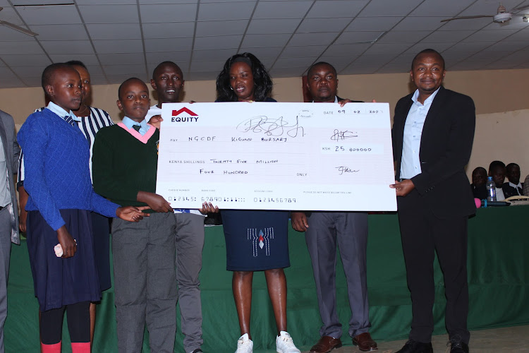 Kigumo MP Joseph Munyoro presents a dummy check of Sh25 million for bursaries at Kigumo Social Hall.