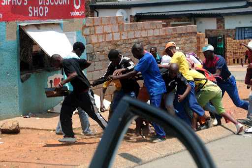 A thief running away with a tray full of cash he had stoeln from a shop in Meadowlands, Soweto. A group of other looters chased him away and he fled into nearby houses.