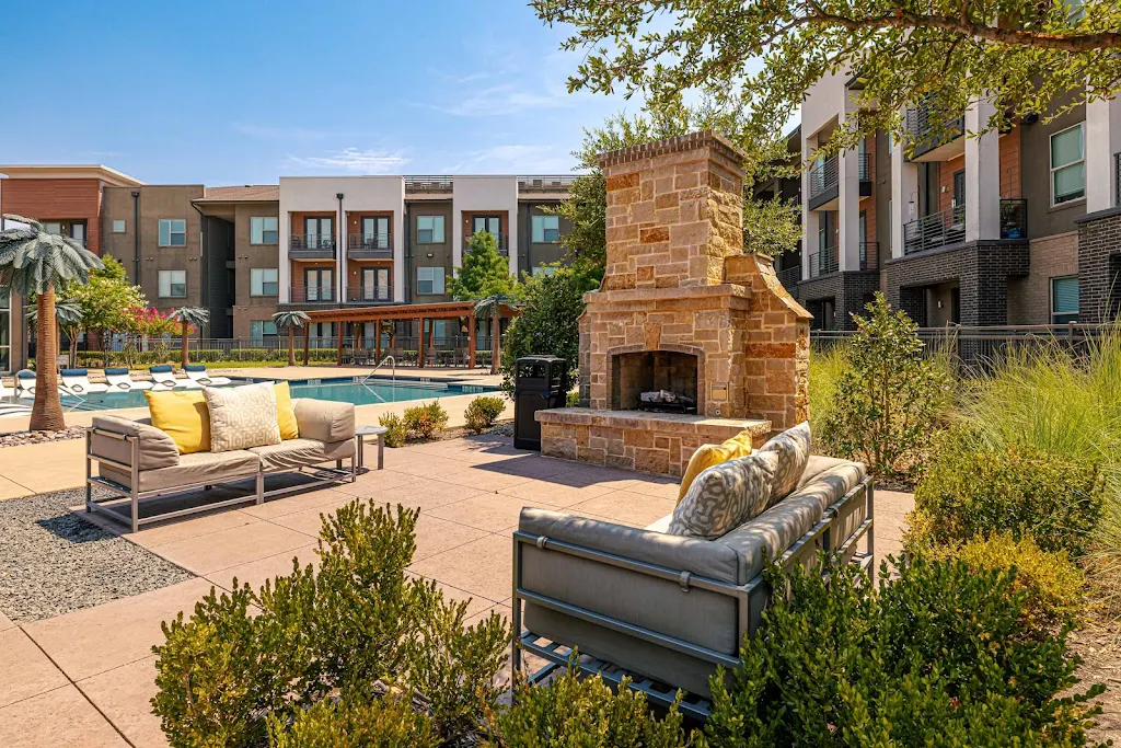 Outdoor stone-inspired fireplace with upholstered conversational seating with the pool & apartment complex in the background.