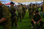 Observant soldiers participate in the 'Mincha' (afternoon) prayer service, near others resting, at a rest stop on October 23 2023 in Southern Israel. Volunteers from across the country have set up rest-stops with snacks, lunch, coffee, drinks and other services for soldiers and police officers. 