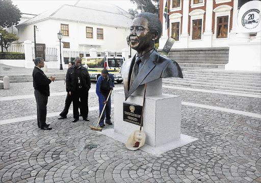 CHIN UP: Cleaners sweep after the new bust of Nelson Mandela outside parliament was hit by a police panel van this week