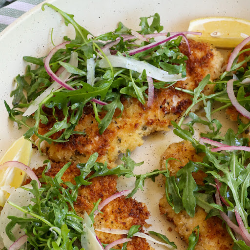 Quick, easy, and elegant Chicken Milanese combines crisp breaded pan-fried chicken breasts with a simple arugula and red onion salad tossed with a simple lemon dressing and topped with Parmesan shavings.