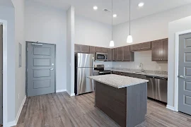 Entry, kitchen, with light grey walls, dark wood floors, stainless steel appliances, island, grey speckled granite countertop