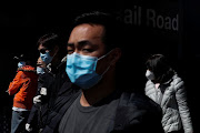 People wearing face masks walk down Main street in Queens, New York, on March 26 2021. 