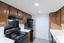 Kitchen with white walls, can lights, and grey wood flooring. White countertops, dark wood cabinets,and black appliances