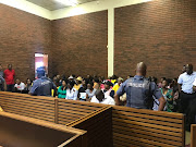 Police officers keep watch over members of the public at the Lenasia Magistrate’s Court, where a 61-year-old man faces seven charges of murder, following the killing of a family in Vlakfontein, south of Johannesburg. 