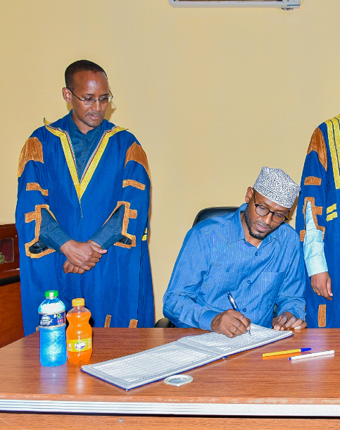 Wajir Governor Ahmed Abdullahi signs the visitors book at the Wajir county assembly. Looking on is assembly speaker Abdille Yuusuf.