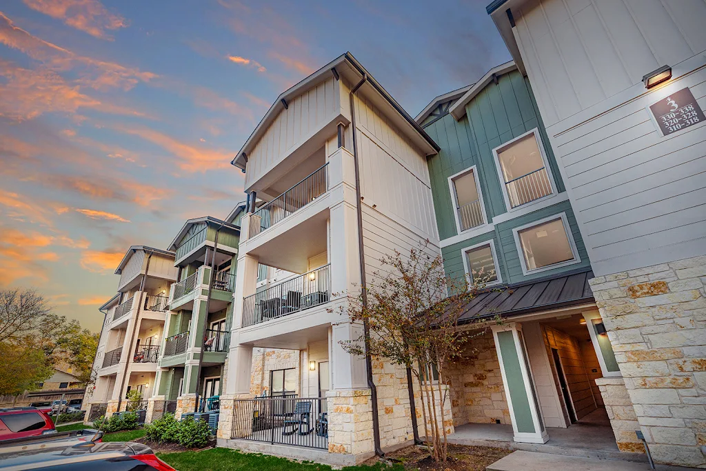 Green, tan and light stone exterior of apartment building at dusk