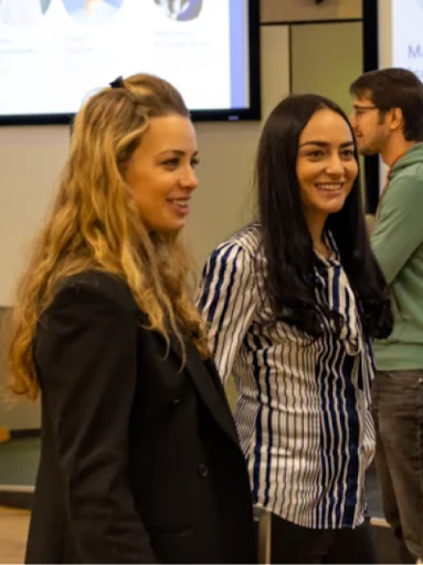 Two women stand talking in a room at a Google for Startups event, a man walks past in the background.