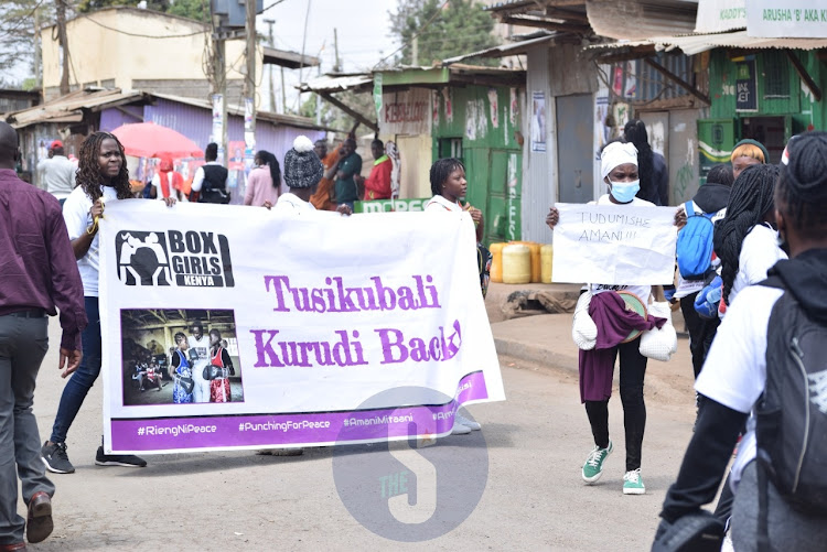 Young women from Boxgirls Kenya display placards with messages of advocating for a peace aheads of the August 2022 polls while on a procession at Kibera on August 2022 polls while on a procession at Kibera on July 27, 2022.