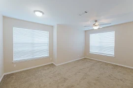 Neutral color scheme in living room with carpet flooring, two large windows with blinds, dome light and ceiling fan